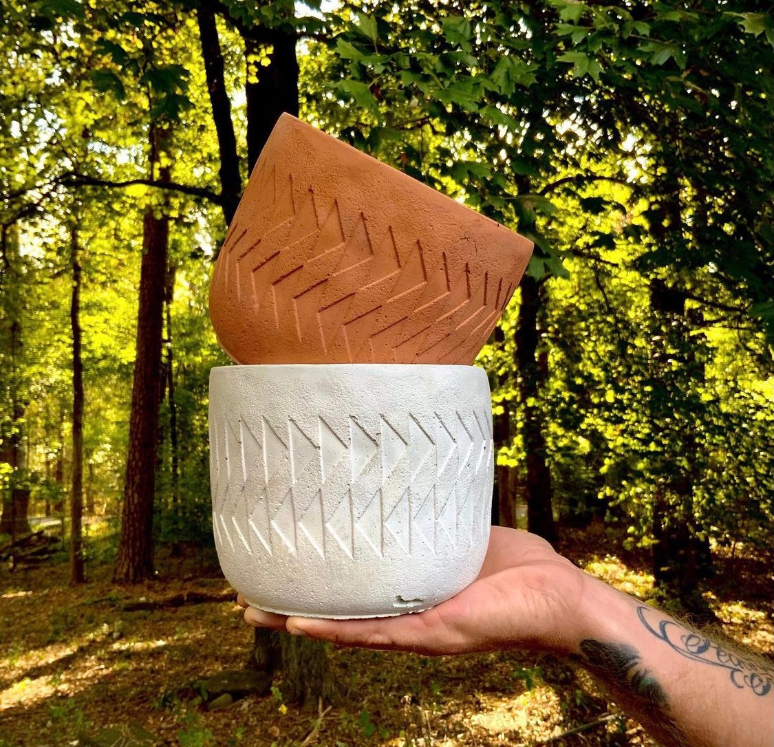 Two different colors of the Arlo planter sit stacked on an outstretched hand, in front of a forest background.