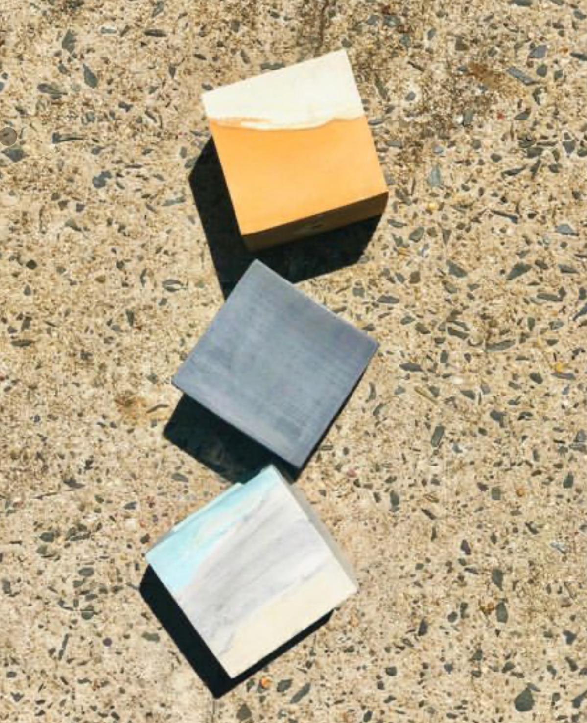 Three 6” concrete cube planters, handmade by Queen City ‘Crete,  lie flat on a concrete background.