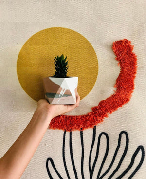 A custom Amelia Geometric Planter, handmade by Queen City ‘Crete, holds a tiny succulent in it, against a bohemian backdrop.